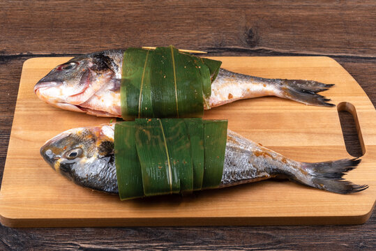 Two raw dorado fish in sauce and bamboo leaves on a cutting board.
