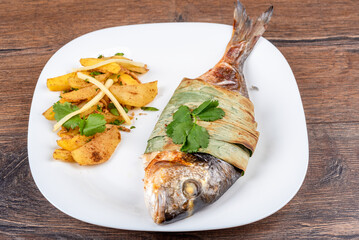 Plate with baked dorado fish and potatoes.