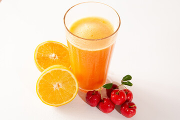 Fresh Organic Acerola and Orange Juice in a glass cup with half orange and acerola berries in a white clean studio photo in top view