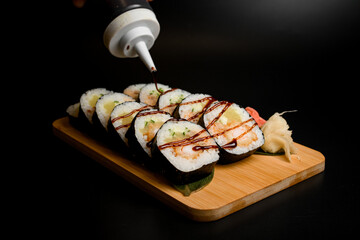Sushi rolls on a wooden board are covered with sauce