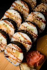 Sushi rolls on a wooden board with sauce and sesame close up