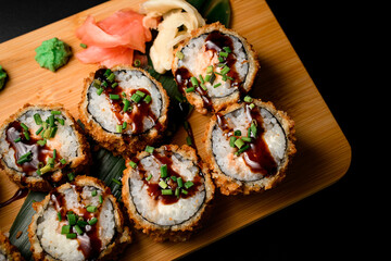 Sushi rolls with sauce on a wooden board served with ginger and wasabi close up