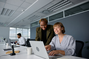 Three young multiracial business people in businesswear smiling and typing on laptop at desk in office