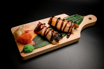 Rolls wrapped in salmon slices drizzled with sauce on a banana leaf
