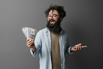 Joyful hipster in glasses displaying a fan of dollar bills, expressing excitement over financial...