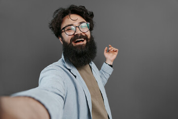Obraz premium Delighted bearded man in casual wear taking a selfie, laughing and enjoying the moment, dark background