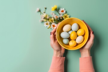 Hands holding bowl with colorful painted Easter eggs, against a light green blue background with flowers. Top view. Banner with copy space. For Easter promotions or spring-themed culinary content.