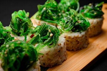 Portion of sushi rolls with a pile of green algae, close up