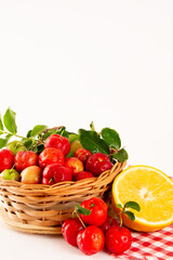 Fresh Organic Acerola and Orange Juice in a glass cup with sliced orange fruit and acerola berries in a bamboo basket in white background in front view