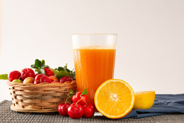 Fresh Organic Acerola and Orange Juice in a glass cup with sliced orange fruit and acerola berries in a bamboo basket in white background in front view