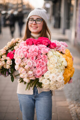 Cute woman holding huge bouquet of multi-colored roses on blurred road background