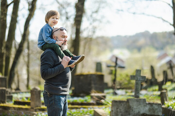 Cute toddler boy and his father admiring blue scilla siberica spring flowers blossoming in April in Bernardine cemetery in Vilnius, Lithuania. - obrazy, fototapety, plakaty