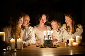 Cute fifteen years old girl making a wish before blowing candles on her birthday cake. Family of...