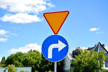 Road sign informing about give way priority and warrant driving right and residential buildings in...
