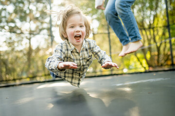 Cute little boy jumping on a trampoline in a backyard on warm and sunny summer day. Sports and...