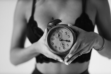 Vintage clock in female hands against breasts in black lingerie