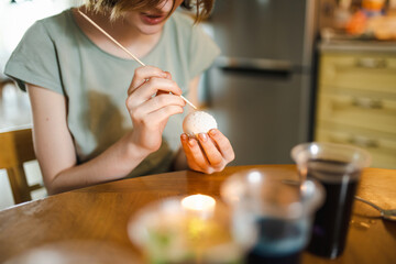 Pretty teenage girl dyeing Easter eggs at home. Child painting colorful eggs for Easter hunt. Kid...