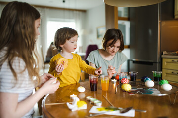 Two big sisters and their little brother dyeing Easter eggs at home. Children painting colorful...