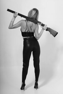 Slender woman in lingerie holding vintage shotgun from the back
