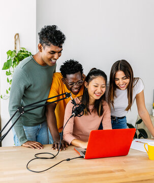 Young group of student friends having fun doing podcast using laptop at home. Teamwork and community concept with diverse millennial content creator people live streaming.
