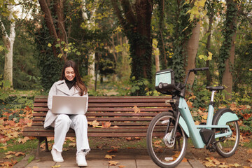 Brazilian beautiful young woman using a laptop in park. She has a bike leaning next to her.
