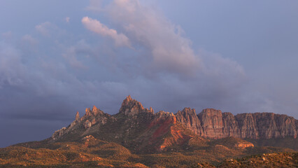The rugged sandstone peaks of Eagle Crags near Zion Nat. park, Utah, USA catches the last of the sunset light as storm clouds drift past in the darkening sky.