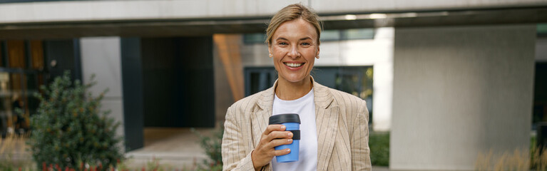 Female manager going to work while drinking coffee on office building background. High quality photo