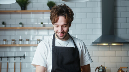 Portrait of happy man with curly hair with in an apron at home in a modern kitchen 