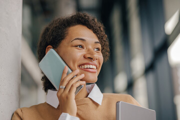 Smiling female freelancer is talking phone with client while standing on coworking background