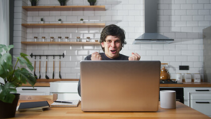 Happy man sitting in the kitchen checking messages read notice receive good news on laptop in...