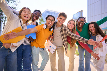 Obraz premium A large multiracial group of teenagers taking a selfie looking front camera laughing and having fun piggybacking together outdoor. Young students enjoying their free time with friends in street city