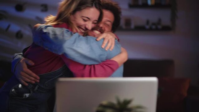 Young Caucasian couple hugging excited celebrate end of project on laptop at night home. Happy people finishing day, closing online project. Married sending important email computer in living room. 