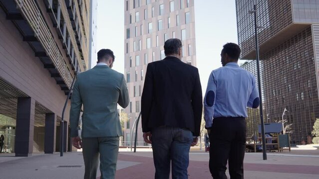 Back view three business men walking for city outside office in financial center. Place of work, planning and discussing new project, professionals job team. Enterprising people have chat on street.