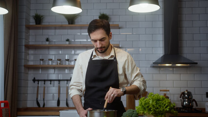 Handsome man cooks soup at home in modern kitchen