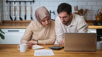 Married couple sitting in kitchen with laptop pay bills, use calculator count expenses, manage finances, make budget control, feel stressed	
