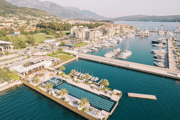 Fototapeta na wymiar Long swimming pool on the wide pier of a luxury marina with moored yachts and modern houses on the shore