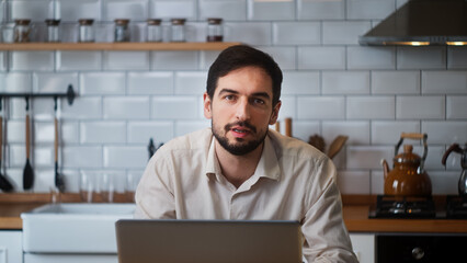 Young handsome businessman talking to the camera while sitting in the kitchen. Motivational speech, business ideas concept	
