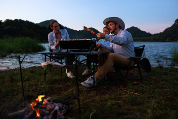 happy family camping party with BBQ, and grilled fish and wine by the  riverside, at evenning,
