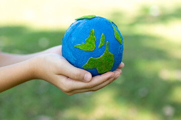 Young boy's hand holding planet Earth globe at natural park background as Earth day to save this planet with ESG principle and environment friendly energy for brighter future. Gyre