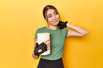 Fit woman holding a protein shake touching back of head, thinking and making a choice.