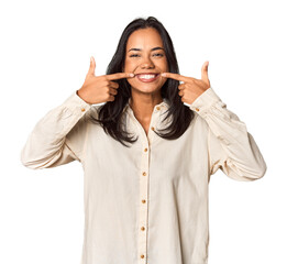 Young Filipina with long black hair in studio smiles, pointing fingers at mouth.