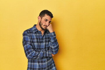 Young Hispanic man on yellow background who feels sad and pensive, looking at copy space.