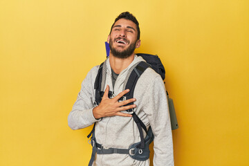 Young Hispanic man ready for hiking laughs out loudly keeping hand on chest.