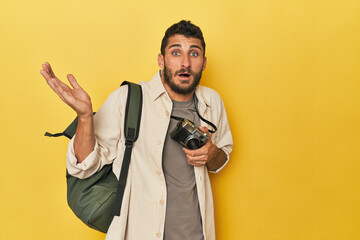Young Hispanic travel photographer poses surprised and shocked.