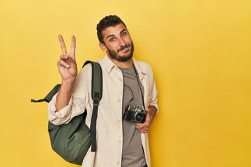 Young Hispanic travel photographer poses joyful and carefree showing a peace symbol with fingers.