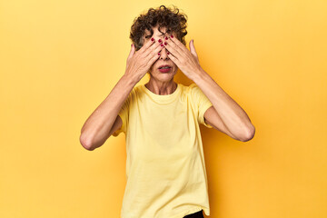 Mid-aged caucasian woman on vibrant yellow afraid covering eyes with hands.