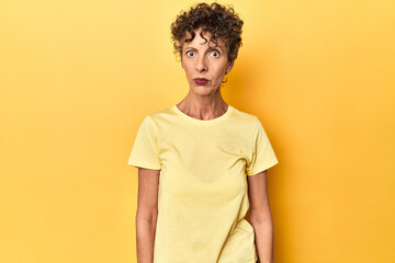 Mid-aged caucasian woman on vibrant yellow sad, serious face, feeling miserable and displeased.