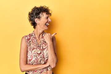 Mid-aged caucasian woman on vibrant yellow points with thumb finger away, laughing and carefree.