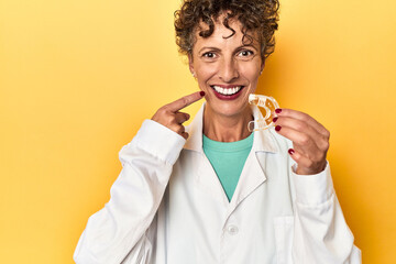 Dental doctor presenting invisible teeth aligner on yellow studio backdrop