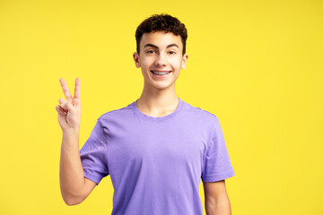 Smiling handsome boy with braces gesturing, showing peace sign with fingers looking at camera © Maria Vitkovska